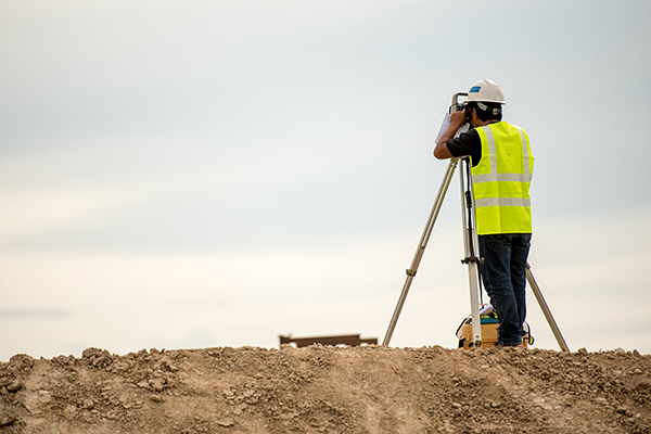Surveyor in a high-vis vest working at the top of a dirt hill.