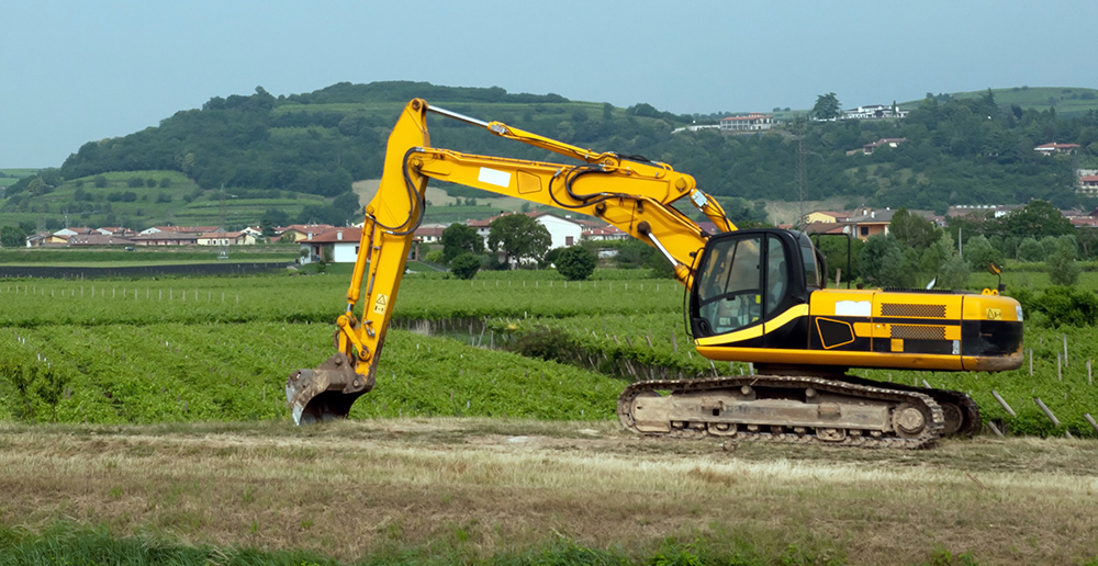 Heavy machinery digging near the edge of a farm property.