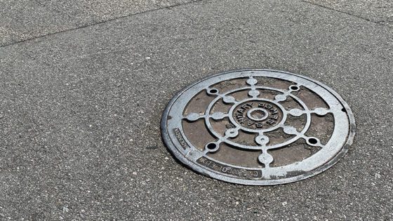 A manhole cover for a sanitary sewer system in an asphalt road.