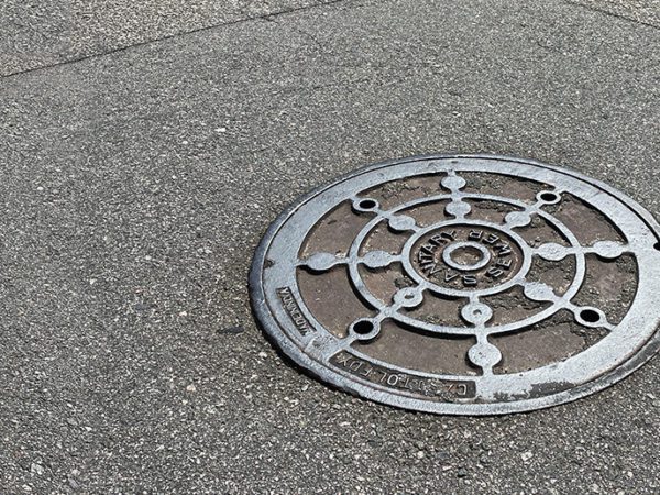 A manhole cover for a sanitary sewer system in an asphalt road.