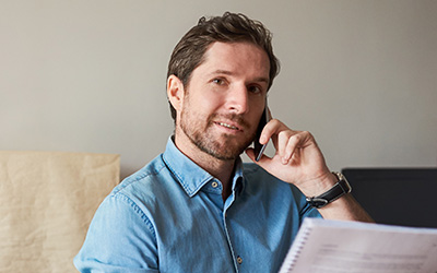 A man smiling on the phone while holding paperwork.