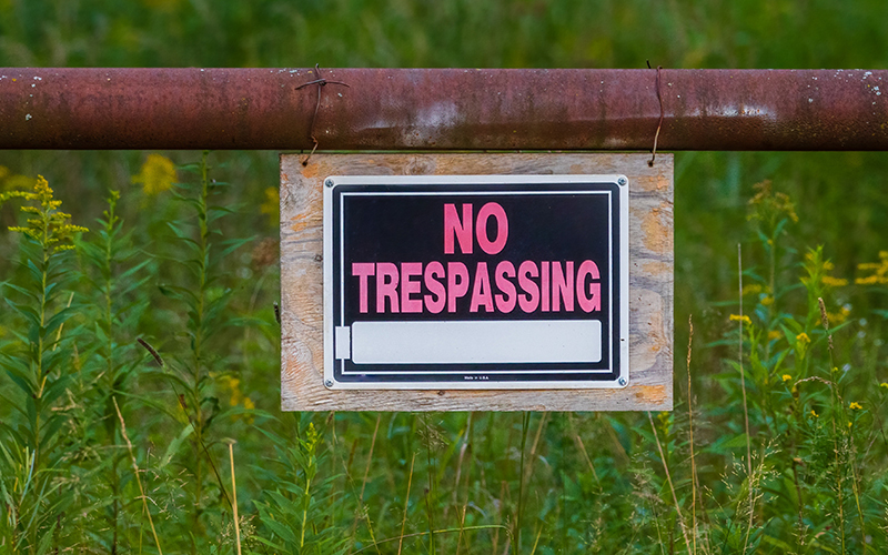 Pink and black no trespassing sign hanging on a rusty metal fence.