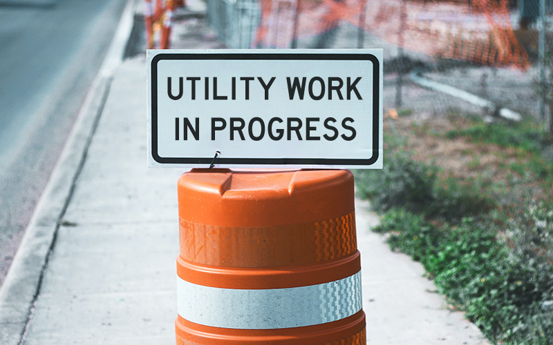 Construction sign reading Utility Work in Progress on an orange barrel.