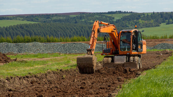 An orange excavator digging in a rural field.