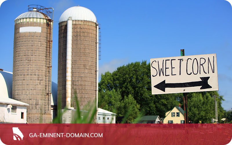 A sign for sweet corn pointing to a farm with two large silos.