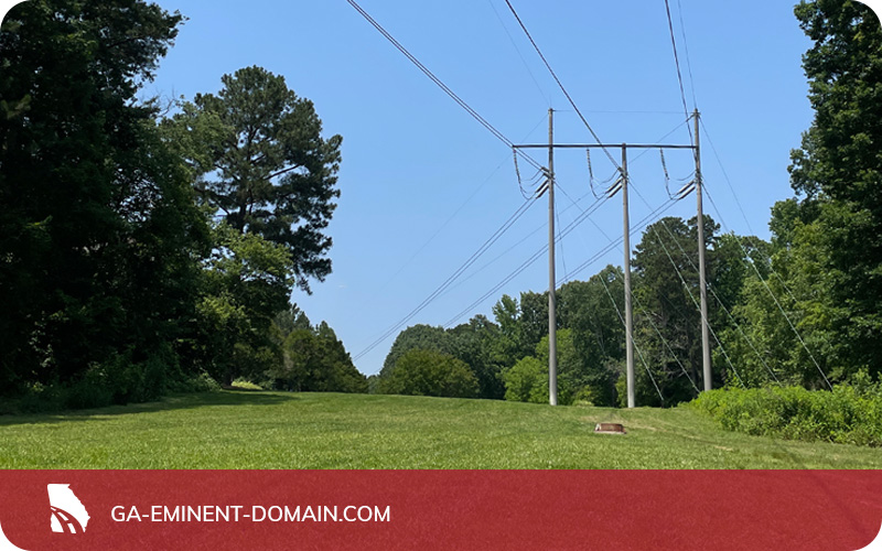 Power lines running over a lawn with trees surrounding and a blue sky above.