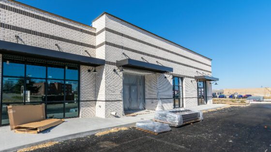 A white brick commercial property in a strip mall with road construction materials on the ground nearby.